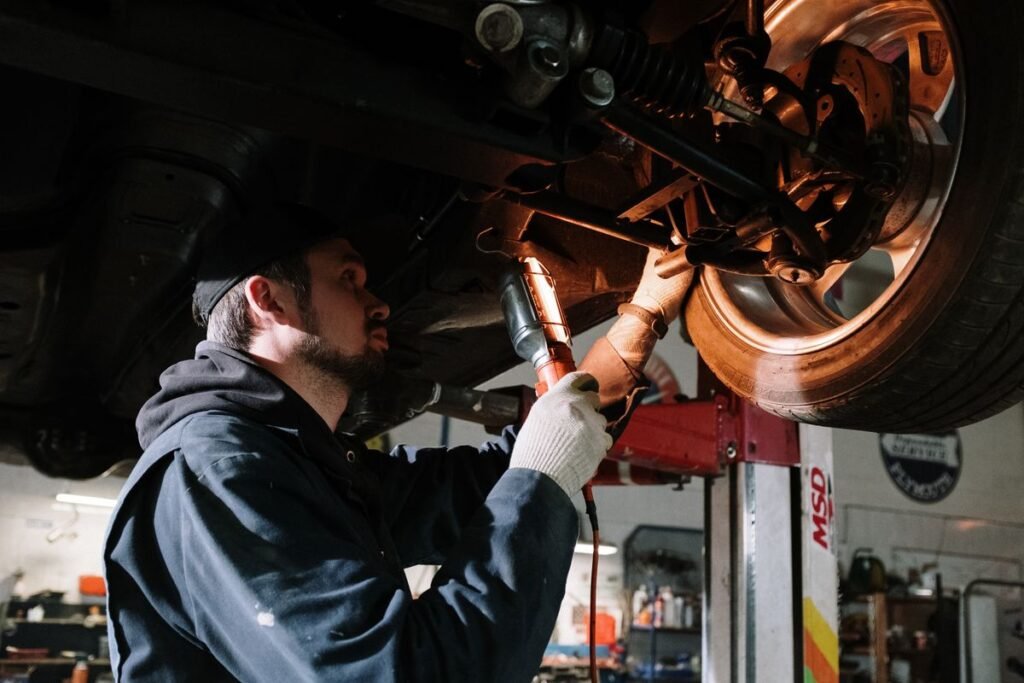 Technician working beneath a raised vehicle with a work light