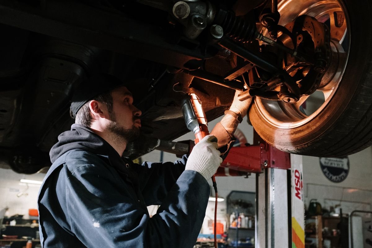 Technician working beneath a raised vehicle with a work light